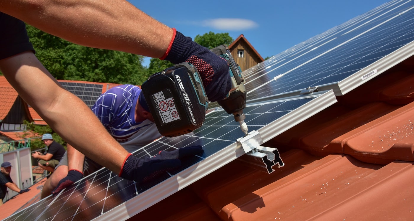 Mitarbeiter einer Firma für Solaranlagentechnik befestigen eine neue Solaranalge auf einem Dach